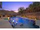 Tranquil pool featuring in-water seating, a waterfall, and vibrant lighting, perfect for evening relaxation at 5 Highland Cove Ln, Henderson, NV 89011