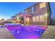 Backyard view of a stunning pool and hot tub illuminated at twilight and covered patio of home at 2787 Donatello Manor Pl, Henderson, NV 89044