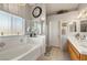 Bathroom featuring tub, double sinks with white countertops, light wood cabinets, and bright natural light from large window at 5950 Mojave St, Pahrump, NV 89061