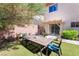 View of backyard featuring artificial grass, an outdoor dining table, patio cover and lush greenery at 135 Manor House Ave, Las Vegas, NV 89123