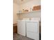 A compact laundry room featuring a white washer and dryer, shelf and basket for organized storage at 7468 Wellfleet Bay Ave, Las Vegas, NV 89179