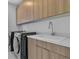 A laundry room featuring front loading washer/dryer, sink and light wood cabinets at 10752 Patina Hills Ct, Las Vegas, NV 89135