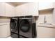 Laundry room with modern cabinets, countertop, sink, and a black front loading washer and dryer at 1429 Iron Hills Ln, Las Vegas, NV 89134