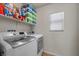 A laundry room with white washer and dryer, storage shelf, and window with blinds at 5656 Fast Payout Ct, Las Vegas, NV 89122