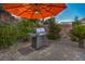 Outdoor grill with orange umbrella, stone patio, and brick wall create a cozy backyard cooking area at 1145 Glacier Park Ct, Henderson, NV 89052