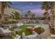 Outdoor living space with a lush backyard featuring a pool with waterfall, palm trees and comfortable seating under ambient lighting at 1246 Diamond Valley St, Henderson, NV 89052