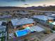 An aerial view showcases a contemporary home with a backyard pool, set against a backdrop of mountains and neighboring houses at 12544 Claymore Highland Ave, Las Vegas, NV 89138