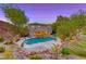 Backyard with a sparkling in-ground pool, mature trees, rock landscaping, and outdoor seating area at 53 Precipice Ct, Henderson, NV 89002