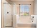 White tiled bathroom with a tub and shower featuring bright natural light from the large window at 11901 Luna Del Mar Ln, Las Vegas, NV 89138