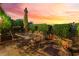 Charming outdoor patio featuring a dining table with an umbrella and lush landscaping against a vibrant sunset sky at 12276 Caminita Pl, Las Vegas, NV 89138