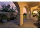 Covered patio with elegant arches and stone flooring, leading to a beautifully landscaped backyard under a colorful sky at 12276 Caminita Pl, Las Vegas, NV 89138