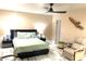 Spacious bedroom with light tile flooring, a ceiling fan, a bed with two side tables and a tan leather chair at 6441 Brushwood Ln, Las Vegas, NV 89107
