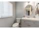 Bathroom features a toilet, sink with gray cabinets, round mirror and a window with blinds at 8484 Montana Stream Ave, Las Vegas, NV 89113