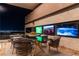 Outdoor dining area with a glass table, stylish seating, and multiple TVs with city views at 720 Dragon Peak Dr, Henderson, NV 89012