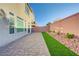 Beautiful paver patio with a strip of faux grass and rock landscaping along the perimeter wall at 7775 Tyrell Peaks St, Las Vegas, NV 89139