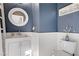 Stylish half-bath features a white vanity and toilet and a round mirror over the sink at 8656 Rowland Bluff Ave, Las Vegas, NV 89178