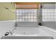 Bright bathroom featuring a soaking tub with tile surround and a glass block window with a bamboo shade at 9909 Masked Duck Ave, Las Vegas, NV 89117