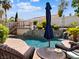 Relaxing poolside view featuring a large blue umbrella, lush landscaping, rock waterfall, and wicker lounge chairs at 1870 Desert Forest Way, Henderson, NV 89012