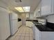 Galley kitchen with white cabinets, black counters, tile floor, and white appliances at 725 Brick Dr, Henderson, NV 89002