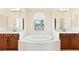 Bright primary bath featuring dual sinks, a soaking tub under a picture window, and tile flooring at 2755 Asgard Ave, Las Vegas, NV 89121
