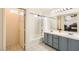 Bathroom features a tub, dual sinks, neutral tiles, bright lighting, and a connected toilet for a spa-like experience at 10413 Rising Harbor Ave, Las Vegas, NV 89129