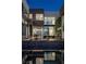 Modern home with a sleek pool reflecting the architecture, lush green wall, and city lights at dusk at 1491 Reims Dr, Henderson, NV 89012