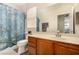 Bathroom vanity with wood cabinets, large mirror, and toilet with floral shower curtain at 1798 Lakewood Dr, Henderson, NV 89012