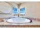 Close-up of a modern soaking tub with marble tile surround and a bright window view at 9628 Matanzas Creek Ct, Las Vegas, NV 89139