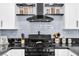 Close-up of the kitchen featuring modern range hood, stainless steel gas range, and decorative open shelving at 6536 Pleasant Plains Way, Las Vegas, NV 89108