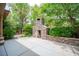 Beautiful backyard showcasing an outdoor stone fireplace, manicured bushes, and concrete patio, surrounded by lush green trees at 15 Emerald Dunes Cir, Henderson, NV 89052
