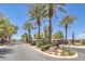 Landscaped median with palm trees and greenery leads to a gated community entrance under a clear blue sky at 6821 Sleepy Pine St, Las Vegas, NV 89130