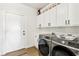 Laundry room featuring a washer, dryer, storage cabinets, wood-look floors, and exterior access at 9410 Stone Castle Way, Las Vegas, NV 89123