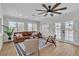 Bright living room with a leather sofa, ceiling fan, wood flooring, and natural light from the large windows at 2532 Big Timber Dr, Las Vegas, NV 89134