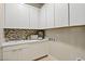 Bright laundry room features white cabinets, decorative backsplash, and practical sink area at 344 Tigullio Ave, Henderson, NV 89011
