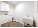 A utility laundry room with a utility sink, upper storage cabinet, and wood-look vinyl flooring at 6101 Cavalry Trl, Pahrump, NV 89060