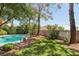 Backyard featuring a blue pool, grass area, and lush landscaping with mature trees and perimeter fencing at 3320 Indian Moon Dr, Las Vegas, NV 89129
