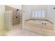 Bright bathroom featuring a luxurious soaking tub, walk-in shower with glass block wall, and tile flooring at 8650 W Verde Way, Las Vegas, NV 89149