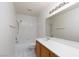 Bright bathroom with white tiled shower and flooring, a wooden cabinet, and a large mirror at 9709 Casper Peak Ct, Las Vegas, NV 89117