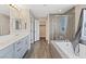 Well-lit bathroom with double sink, large tub, walk-in shower and wood look floors at 10058 Matter Overlook Dr, Las Vegas, NV 89178