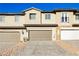A row of townhomes with multi-car garages and neutral color scheme under a bright blue sky at 675 Omaggio Pl, Henderson, NV 89011