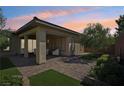 Covered patio with brick pavers, lush landscaping, and comfortable seating area at 10057 Regency Canyon Way, Las Vegas, NV 89148