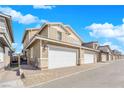 Tan two-story townhome featuring an attached two car garage with stone accents, and a brick paver driveway at 734 Last Dance Pl, Henderson, NV 89011