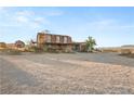 Wide view of a two story home with a large dirt lot in front and outbuildings nearby at 11875 Maggie Ave, Las Vegas, NV 89166