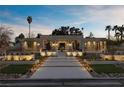 Stunning modern home with landscaped yard, manicured trees, a paver driveway and professional lighting at dusk at 2401 Driftwood Dr, Las Vegas, NV 89107