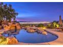 Luxury pool and spa with waterfall feature at twilight, overlooking city lights at 3 Palmbrook Ln, Henderson, NV 89052