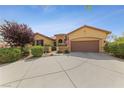 Tan house with a three-car garage and mature landscaping at 10372 Hawks Wing St, Las Vegas, NV 89178