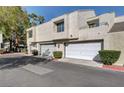 Tan stucco exterior of townhome with white garage doors and landscaping at 8945 Clairton Ct, Las Vegas, NV 89117