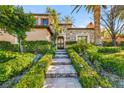 Elegant home entrance with a paved walkway, lush landscaping, exterior lighting, and a custom wrought iron door at 10117 Summit Canyon Dr, Las Vegas, NV 89144