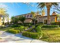 Stunning home exterior with manicured landscaping, stone accents, a custom iron door, and lush, green hedges at 10117 Summit Canyon Dr, Las Vegas, NV 89144