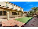 Relaxing backyard featuring a covered patio, artificial turf, stepping stones, and a mature palm tree at 221 Raptors View Ave, Las Vegas, NV 89031